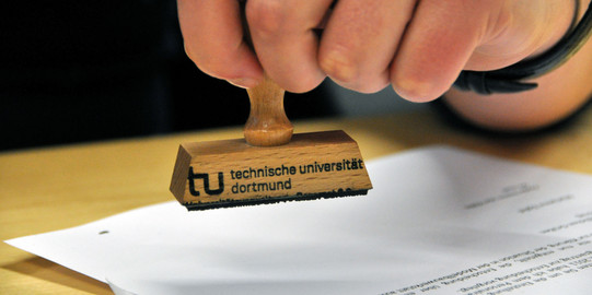 Nahaufnahme einer Hand, die einen Stempel der TU hält.